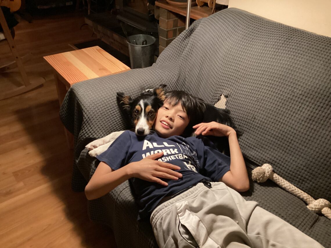 This is a photo of my 11 year old brother lying his head on my 8 month old border collie puppy. She has her head wrapped around my brother's head. They are sprawled across the couch and look relaxed.